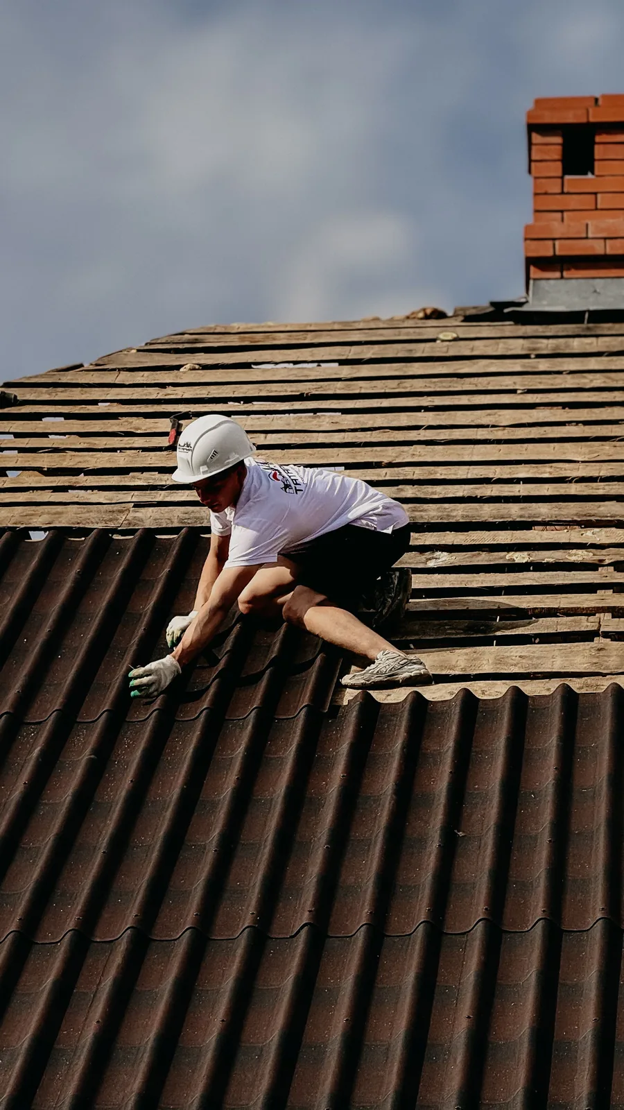 Couvreur casqué posant des tuiles sur une toiture en pente